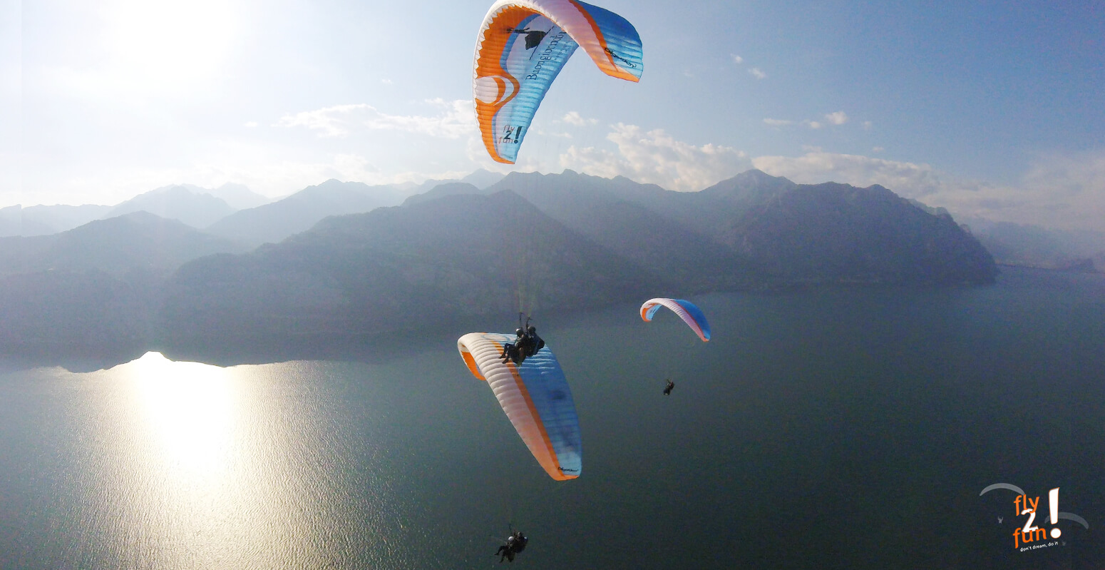 in-questa-immagine-vediamo-un-gruppo-in-parapendio-biposto-pilotati-da-piloti-professionisti-in-volo-sul-lago-di-Garda-nel-mezzo-delle-montagne
